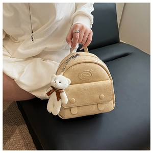 Detail of off-white mini backpack featuring a plush bear charm and heart ribbon accessory