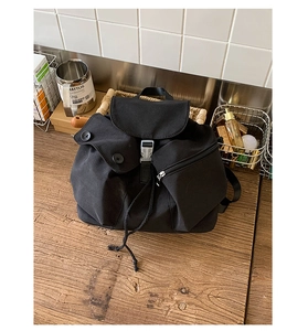 Close-up of black canvas backpack with drawstring closure and buckle on wooden table