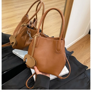 Détail d'un sac seau marron à motif litchi avec un pendentif en cuir en forme d'éléphant