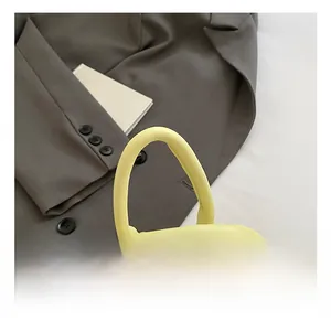 Detail view of cream leather handbag featuring a cylindrical top handle and silver dual zippers