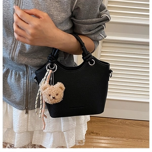Detail of black pebbled leather bucket bag with bear charm and striped scarf accent