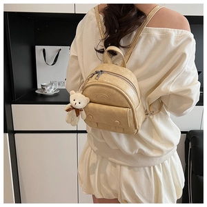 Detail of beige mini backpack with wrinkled texture, twin zippers and a teddy bear charm
