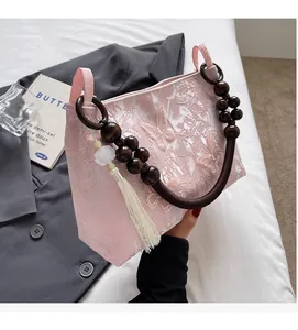 Détail du sac papillon en dentelle rose avec poignée en bois et pompon floral élégant