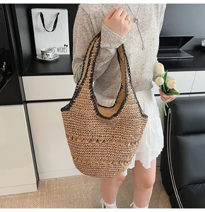 Detail of the woven straw tote bag featuring contrast black trim and sturdy handles