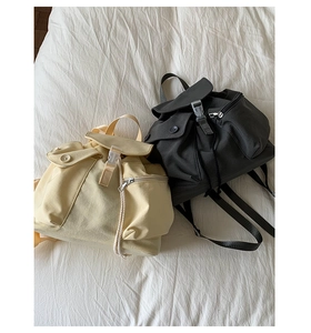 Detail view of beige and dark grey nylon backpacks with buckles and drawstrings
