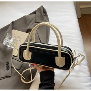 Close-up of minimalist black baguette bag with white contrast piping and top handle detail