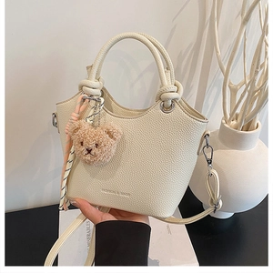 Detail of cream bucket bag with litchi grain texture, bear charm and striped silk scarf