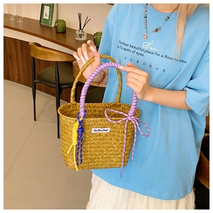 Detail of straw woven bucket bag featuring colorful knotted handles and logo patch