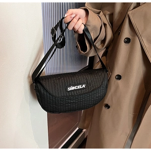Close-up of black quilted crescent saddle bag with wide strap and white SMKCELA logo