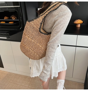 Close-up of hand-woven straw tote bag with black contrast stitching and shoulder strap