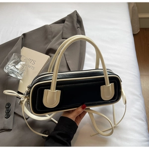 Detail of a chic black and cream leather baguette bag with top handles and adjustable strap