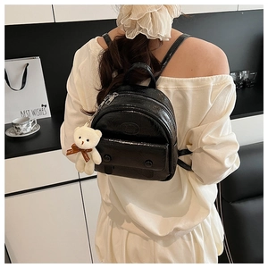 Glossy black mini backpack for women featuring a cute plush bear charm with brown bow