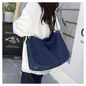 Detail of a large dark blue denim tote bag worn by a model in a modern urban street setting