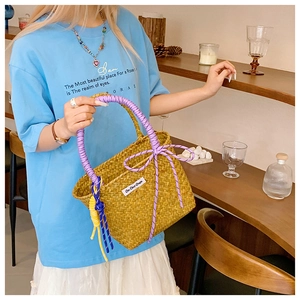 Detail of hand-woven straw bucket bag with purple rope handle and yellow tassel accent