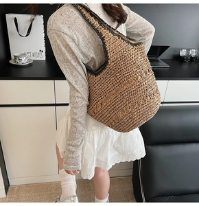Detail of the woven straw texture and black contrast edges on the large summer hobo bag