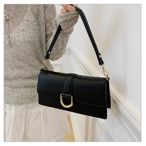 Détail d'un sac à main en cuir noir mat avec boucle dorée en D et texture de qualité