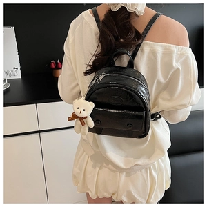 Back view of a mini black vintage backpack featuring a white plush bear charm and glossy finish