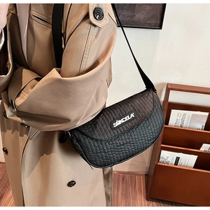 Detail of black quilted saddle bag with adjustable strap on a khaki trench coat