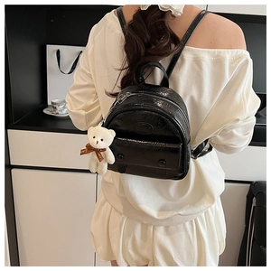 Detailed back view of a glossy black mini backpack with a plush bear charm on a model
