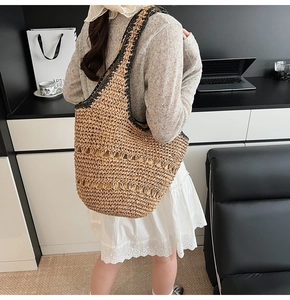 Detailed shoulder view of a large woven straw tote bag with black hollow trim