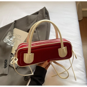 Detail of red leather baguette bag with contrast cream U-shaped accent on a bed