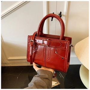 Détail du sac à main en cuir verni bordeaux avec rivets argentés et boucle métallique