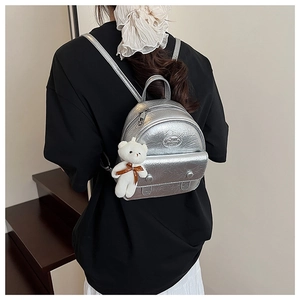 Silver metallic mini backpack with plush bear charm worn at a 45-degree angle