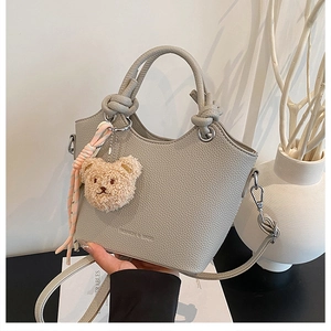 Close-up of gray lychee texture bucket bag with knotted handle and plush bear charm detail
