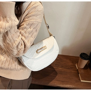 Detail of white quilted saddle bag featuring a gold metal logo and adjustable wide strap