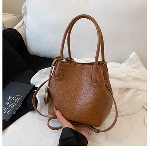 Détail du sac seau en cuir marron à motif litchi avec doubles poignées et fine bandoulière