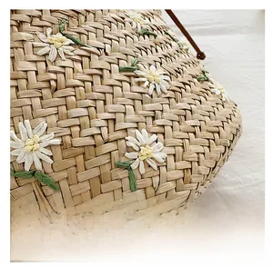 Detail of straw bucket bag featuring embroidered white daisies and brown leather drawstring
