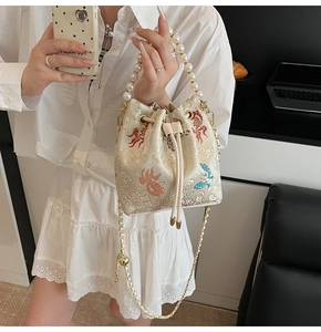Détails de broderie sur sac seau blanc avec poignée en perles et chaîne dorée