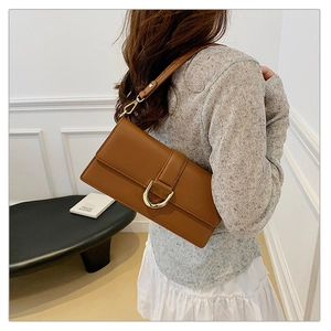 Détail d'un sac bandoulière caramel avec boucle dorée en U porté par un mannequin