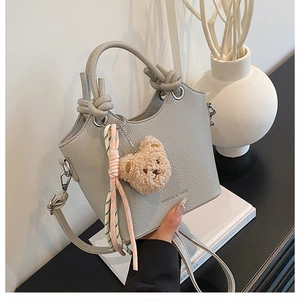 Close-up of light gray pebble leather bucket bag with knotted handle and bear charm