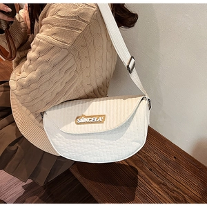 Detail of a creamy white textured saddle bag with wide fabric strap and brand logo