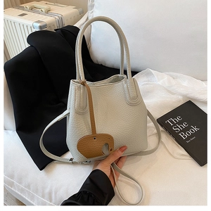 Sac seau motif litchi avec breloque éléphant porté par un mannequin dans un bureau chic