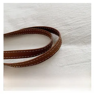 Detail of a brown leather handle with white contrast stitching on a straw tote bag