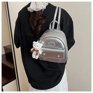 Detail of silver metallic mini backpack with crinkled texture and white teddy bear charm