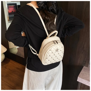 Close-up of white quilted mini backpack with star badge and metal rivets on model