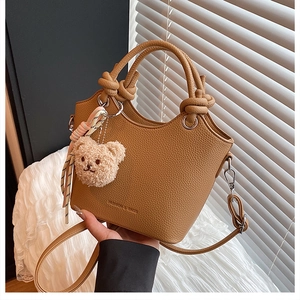 Close-up of brown pebbled leather bucket bag with silk scarf handle and plush bear charm
