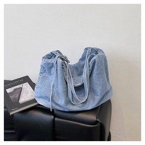 Detailed shot of light blue denim tote bag with metal eyelets on a black surface