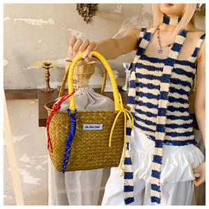 Detail of woven straw bucket bag featuring yellow glossy handle and colorful rope knot
