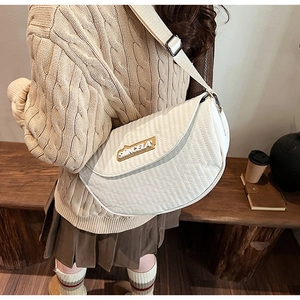 Detailed view of beige quilted half-moon crossbody bag with wide strap on a wooden bench
