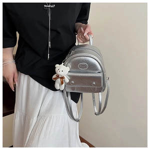 Detail of silver metallic mini backpack featuring crinkled texture and teddy bear charm