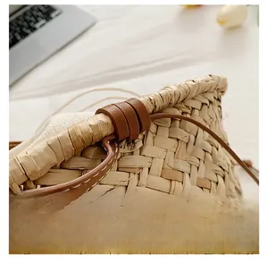 Detail of straw tote bag with leather trim, drawstring, and handmade daisy embroidery