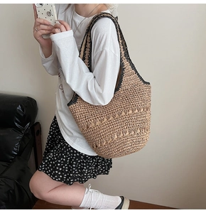 Detail of woven straw tote bag with black trim showing size and drape on a shoulder