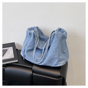Detail view of large light blue denim tote bag with metal eyelets on a black bench