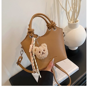Detail of caramel lychee leather bucket bag with knot handles and teddy bear charm