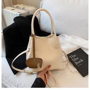 Vue détaillée du sac seau blanc motif litchi avec charm éléphant marron et fine bandoulière