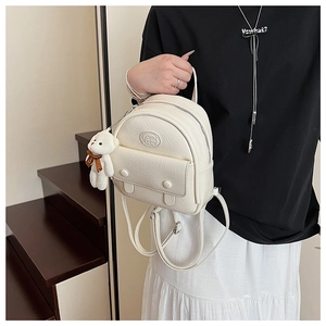 Close-up of white embossed leather mini backpack featuring a plush bear charm and magnetic pocket